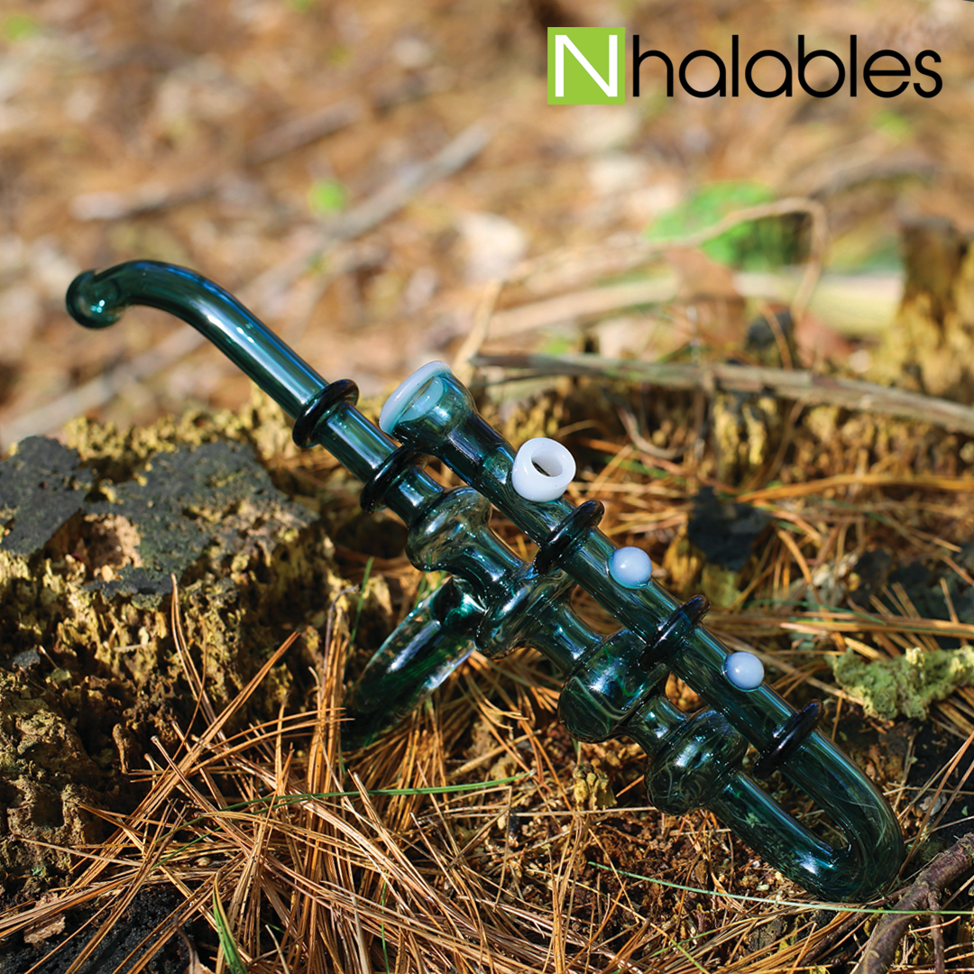 Nhalables Social Post showing a Blue Saxophone waterpipe by New York Based Artist Hawk Glass sitting in a stump with some pine needles around.