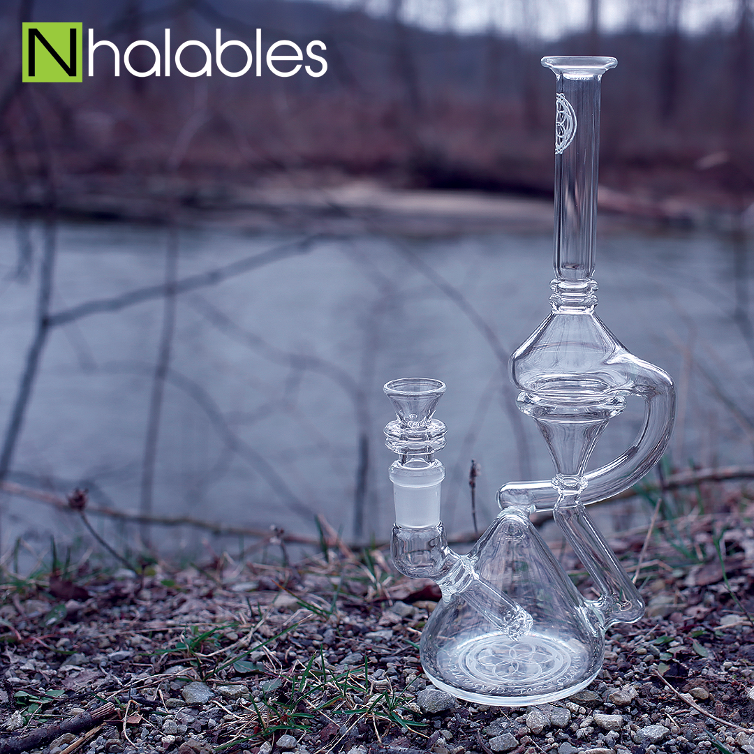 Nhalables Social Post Showing a Tetra-Cycler Oil Rig By Seed Of Life Glassworks sitting on rocks in front of a small river.